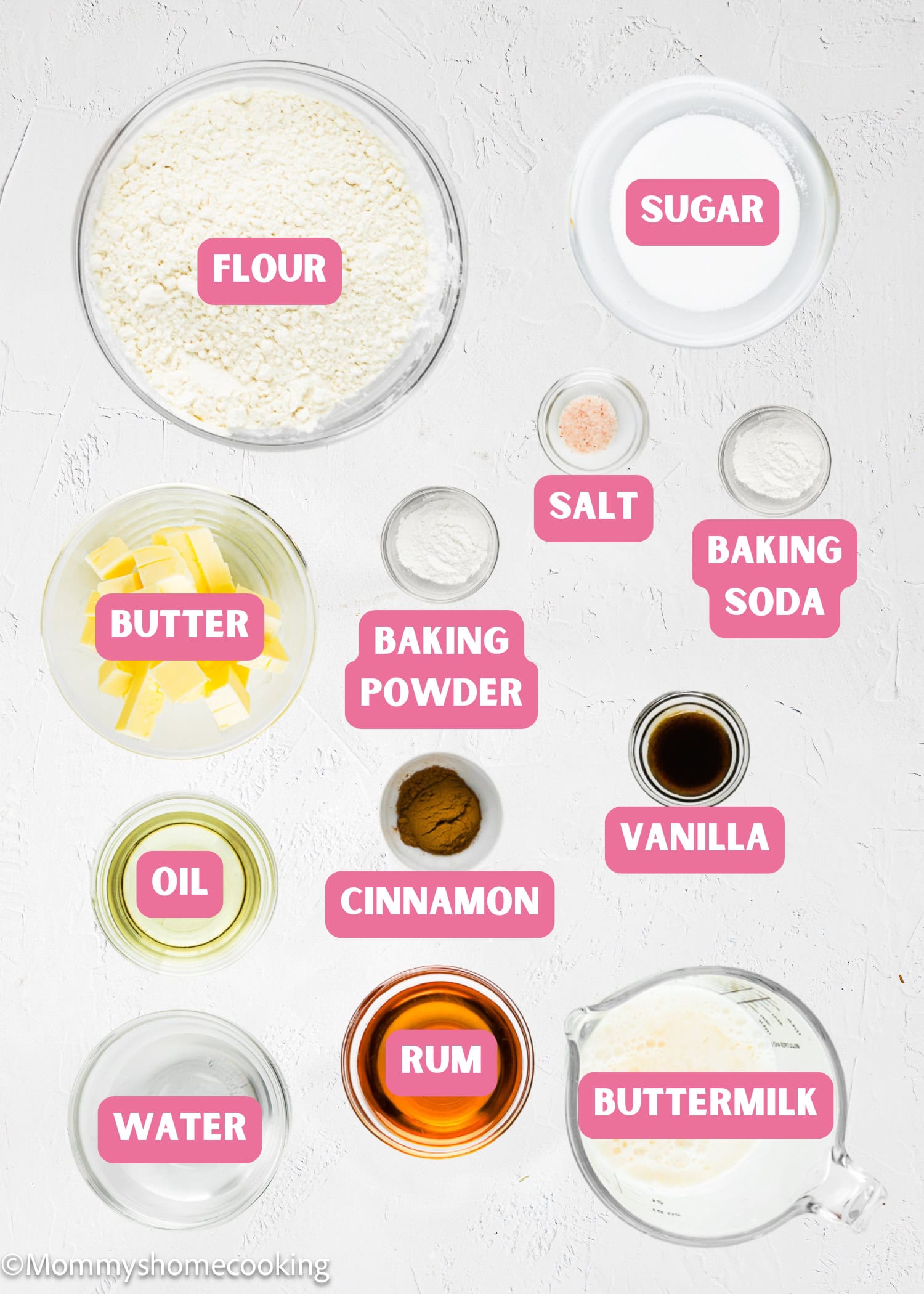 Top-down view of labeled Eggless Butter Rum Bundt Cake vertical ingredients in bowls and containers, including flour, sugar, butter, oil, water, buttermilk, cinnamon, rum, vanilla, salt, baking powder, and baking soda.