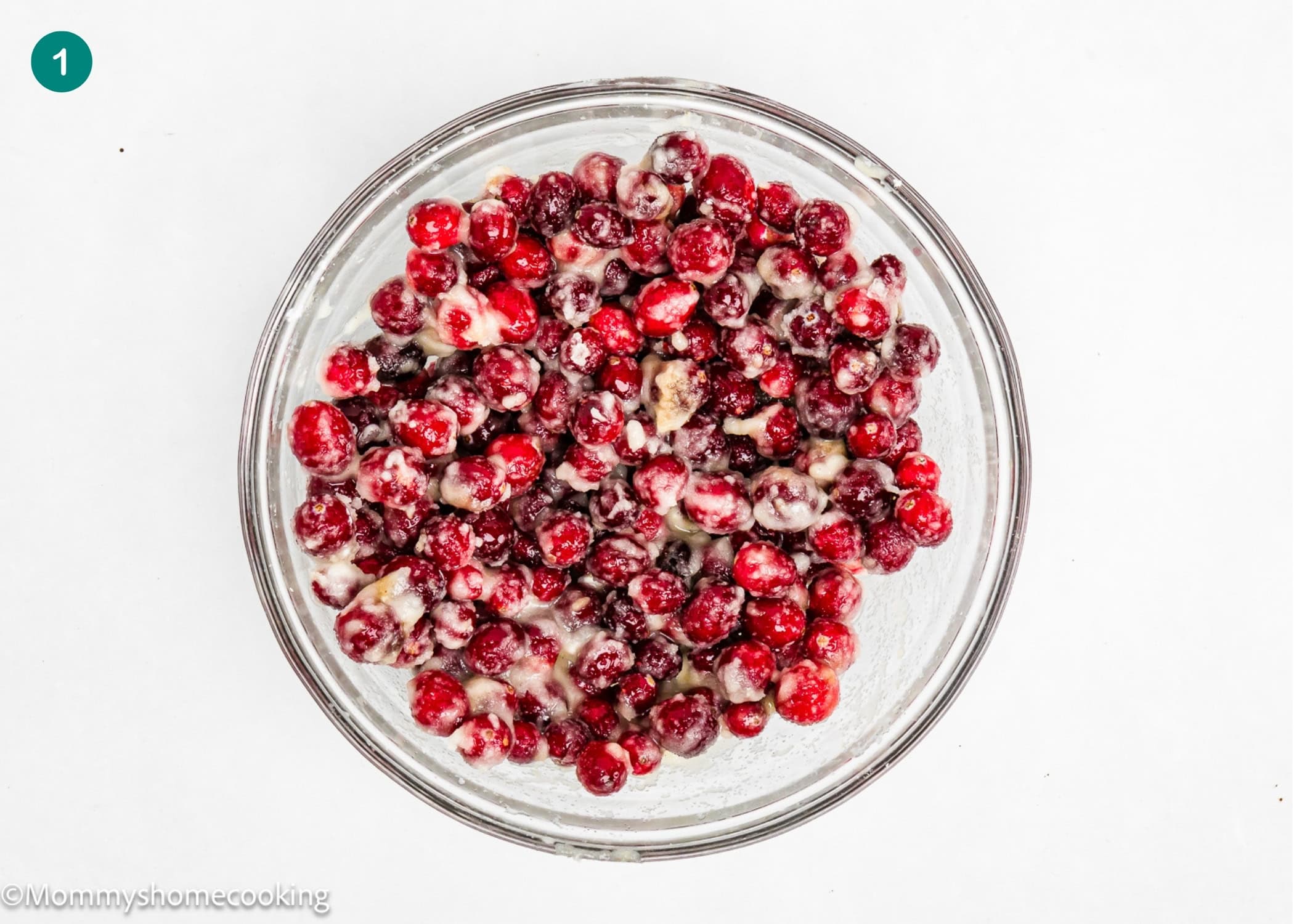 A glass bowl filled with cranberries coated in flour and sugar, a perfect start for Eggless Cranberry Crumble Pie Bars, placed on a white background.