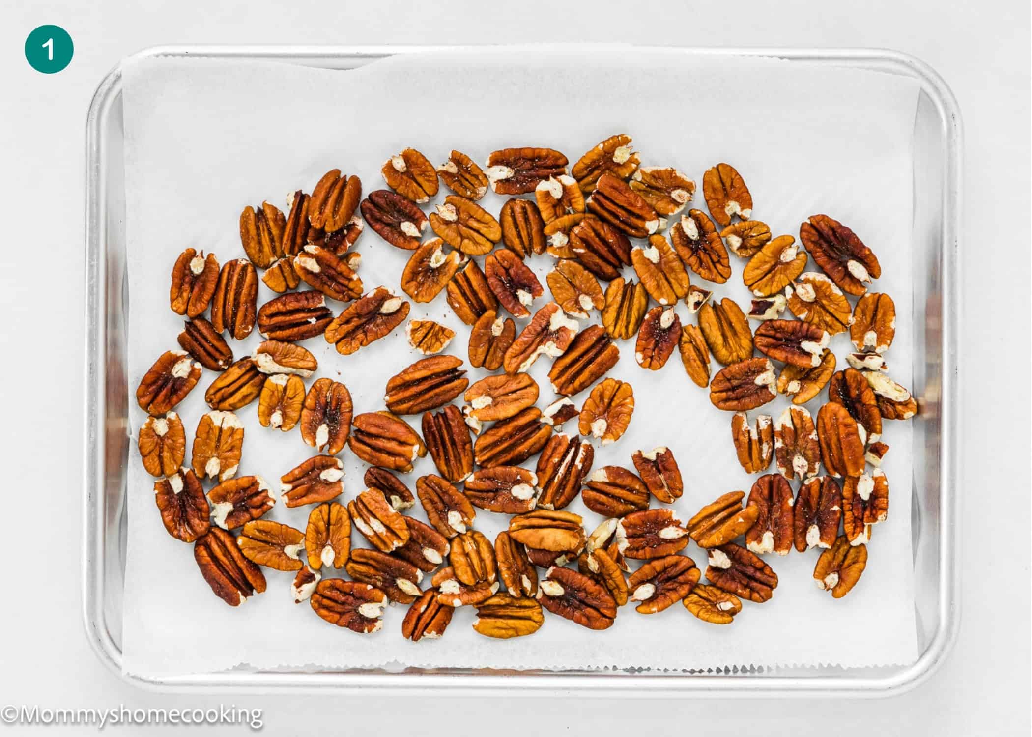 A glass baking dish lined with parchment paper holds a single layer of roasted pecan halves, perfect for topping an Eggless Italian Cream Cake.