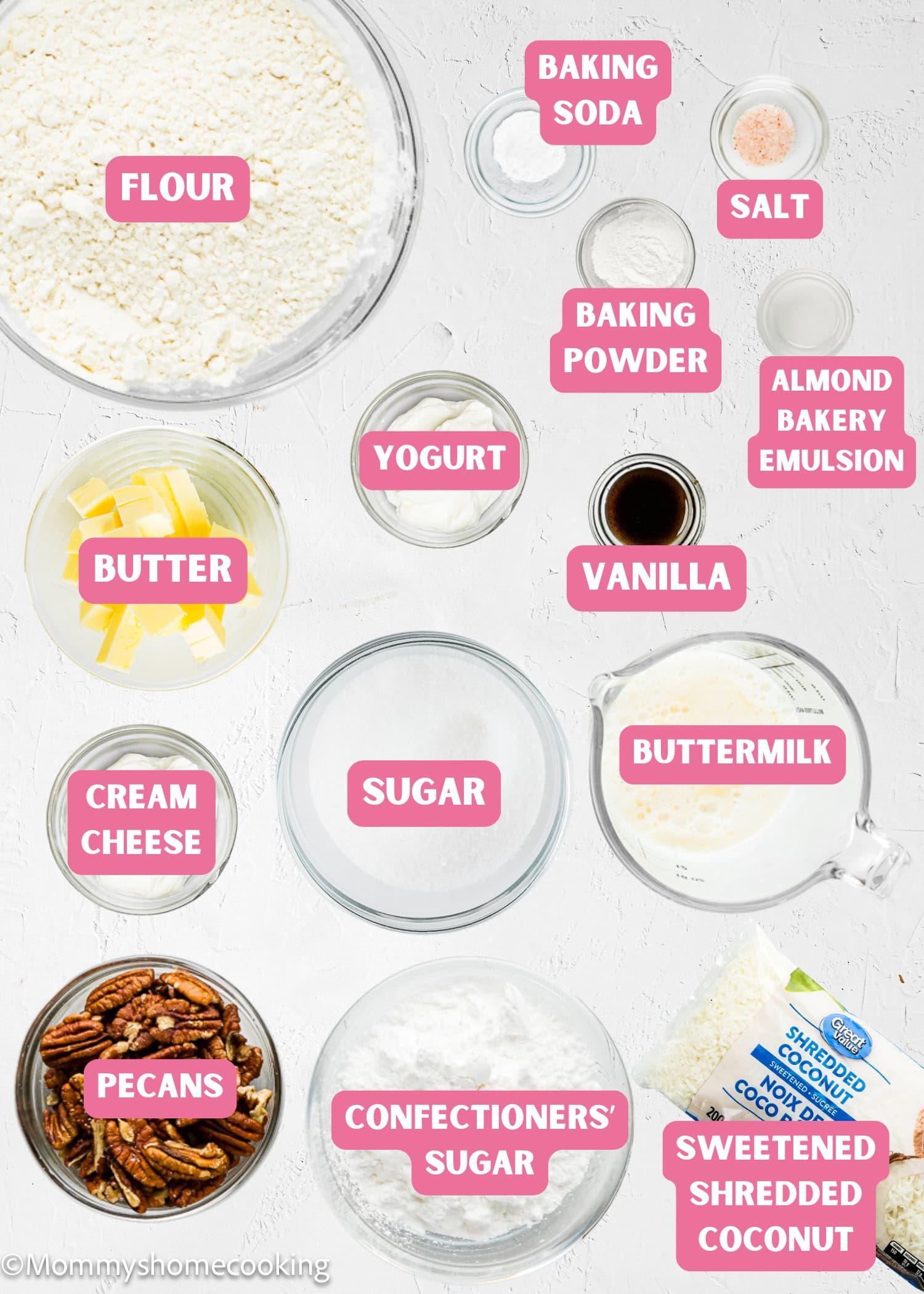 Various baking ingredients labeled in bowls and containers on a white surface, including flour, butter, sugar, yogurt, pecans, baking powder, and shredded coconut—perfect for making an Eggless Italian Cream Cake.