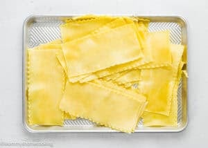 A baking tray filled with uncooked lasagna pasta sheets arranged in overlapping layers.