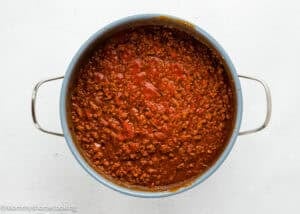 A pot filled with ground meat simmering in tomato-based sauce, viewed from above on a white background.