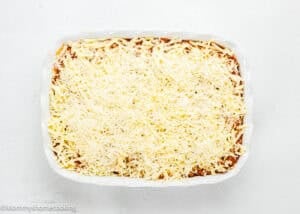 Rectangular baking dish filled with a layered casserole topped with a generous amount of shredded cheese, ready to be baked.