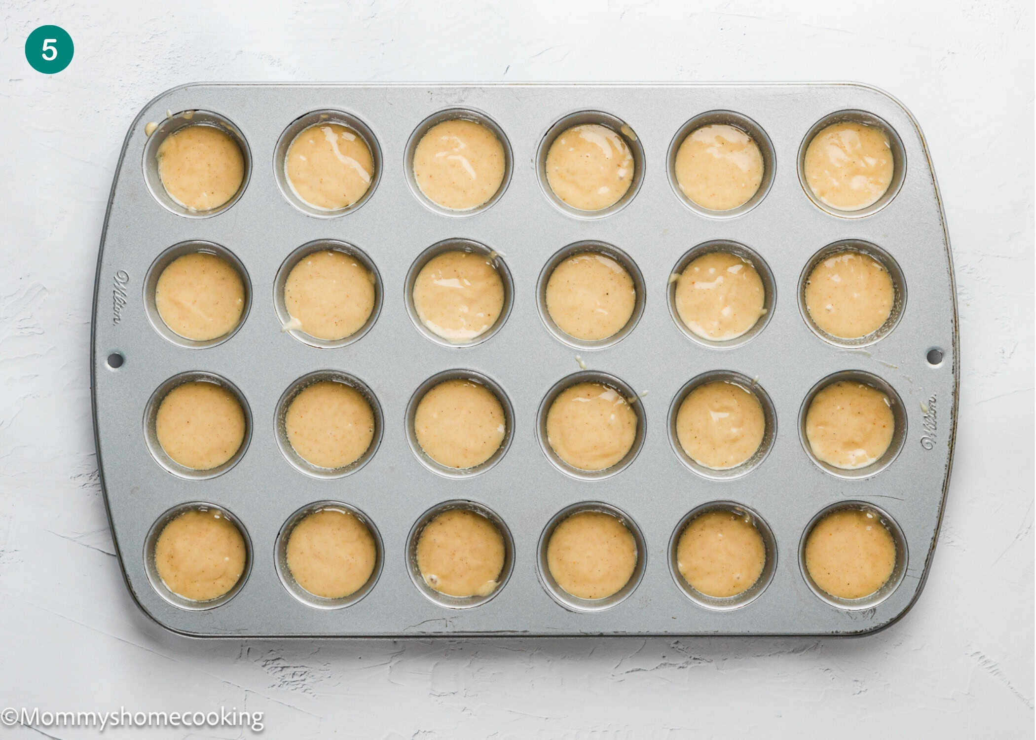 A 24-cup mini muffin pan is filled with batter for Eggless Mini Powdered Sugar Donut Muffins, ready to be baked.
