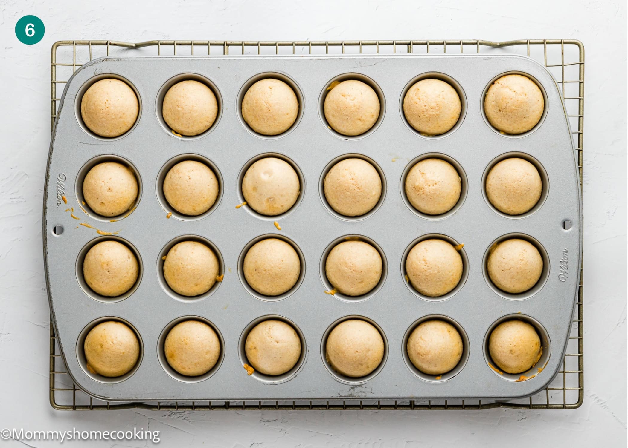 A metal muffin pan with 24 Eggless Mini Powdered Sugar Donut Muffins sits on a wire cooling rack, viewed from above.