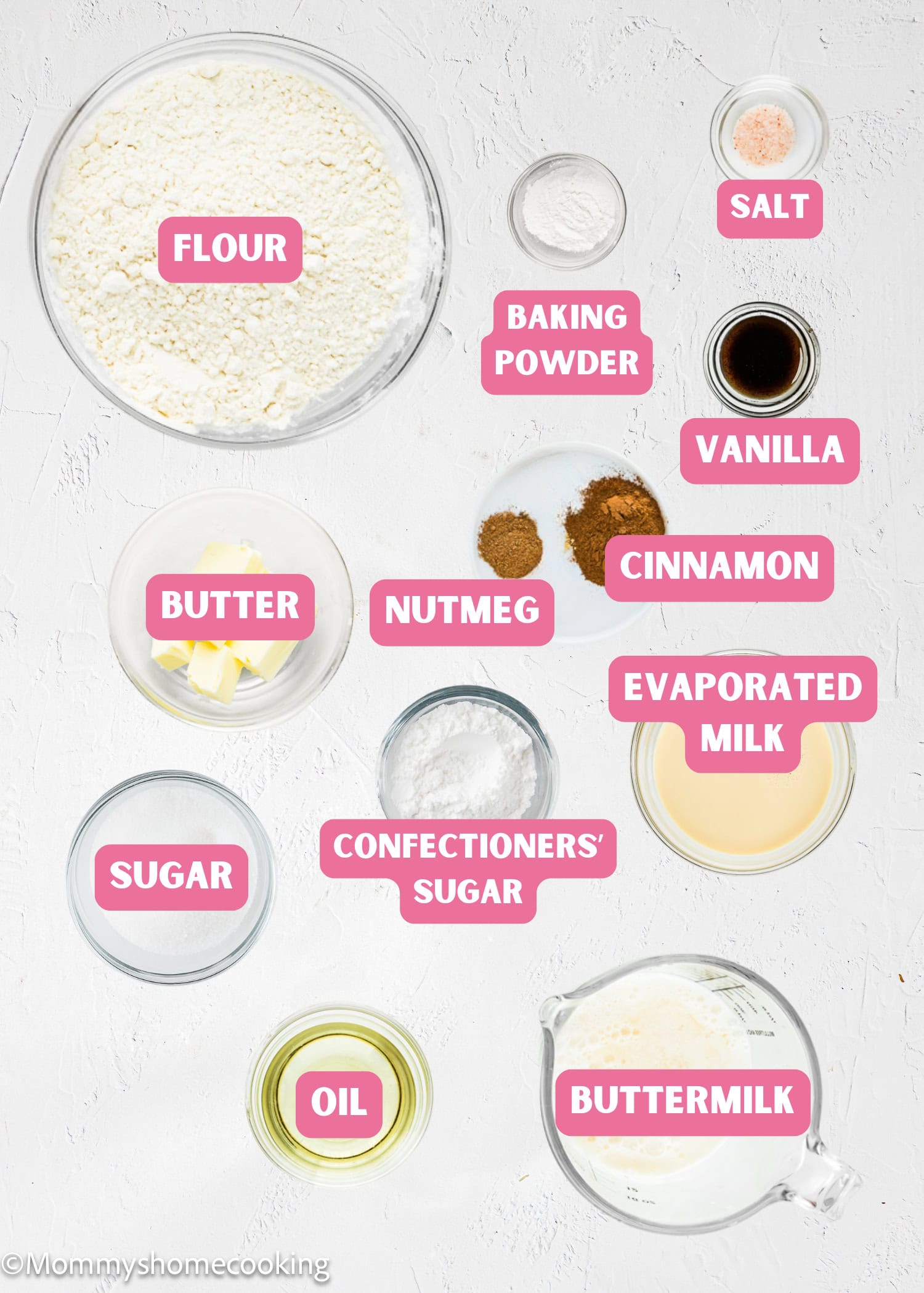 Overhead view of baking ingredients in bowls labeled flour, sugar, butter, oil, baking powder, salt, nutmeg, cinnamon, vanilla, evaporated milk, buttermilk, and confectioners' sugar for Eggless Mini Powdered Sugar Donut Muffins.