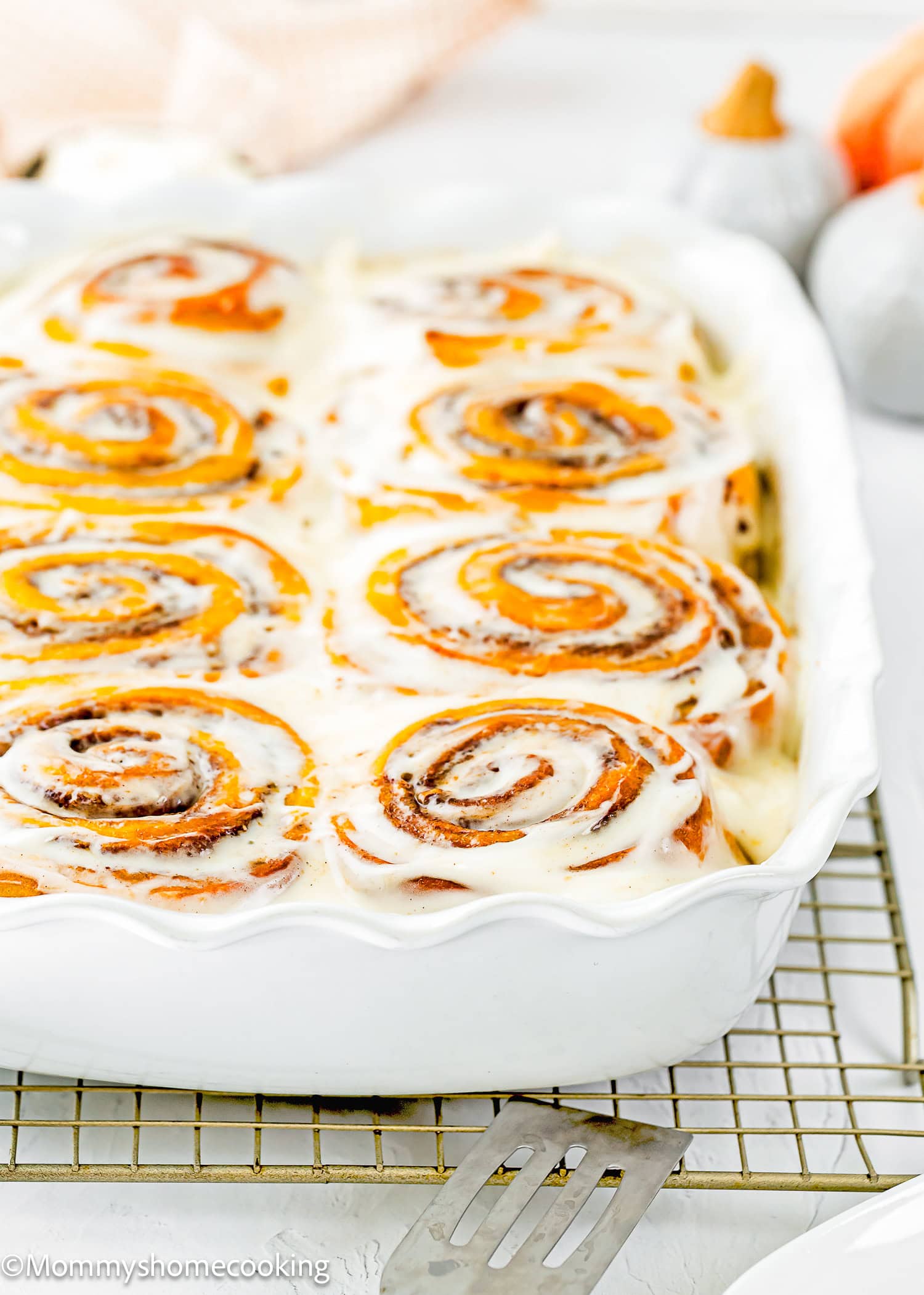 An eggless pumpkin cinnamon roll on a baking dish with small bowls of ingredients in the background.