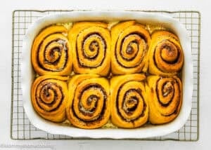 Baked eggless pumpkin cinnamon rolls in a baking pan over a cooling rack.