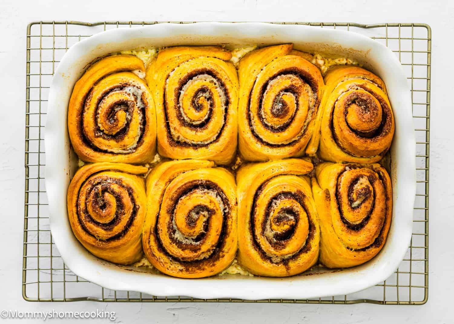 Baked eggless pumpkin cinnamon rolls in a baking pan over a cooling rack.