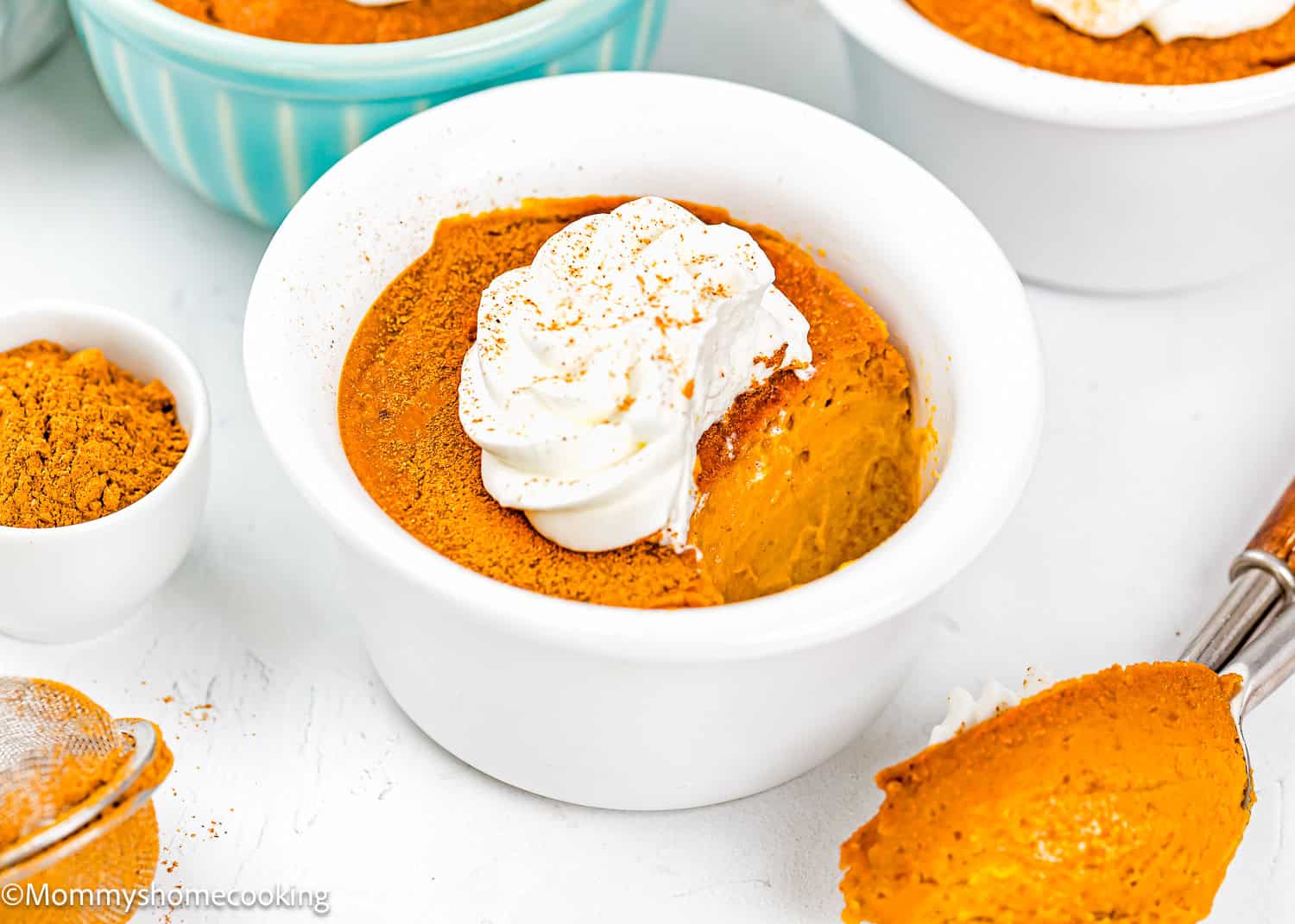 Eggless Pumpkin Custard Cups (Crustless Pumpkin Pie) topped with whipped cream and a sprinkle of cinnamon, served in a white ramekin with a spoonful on the side.