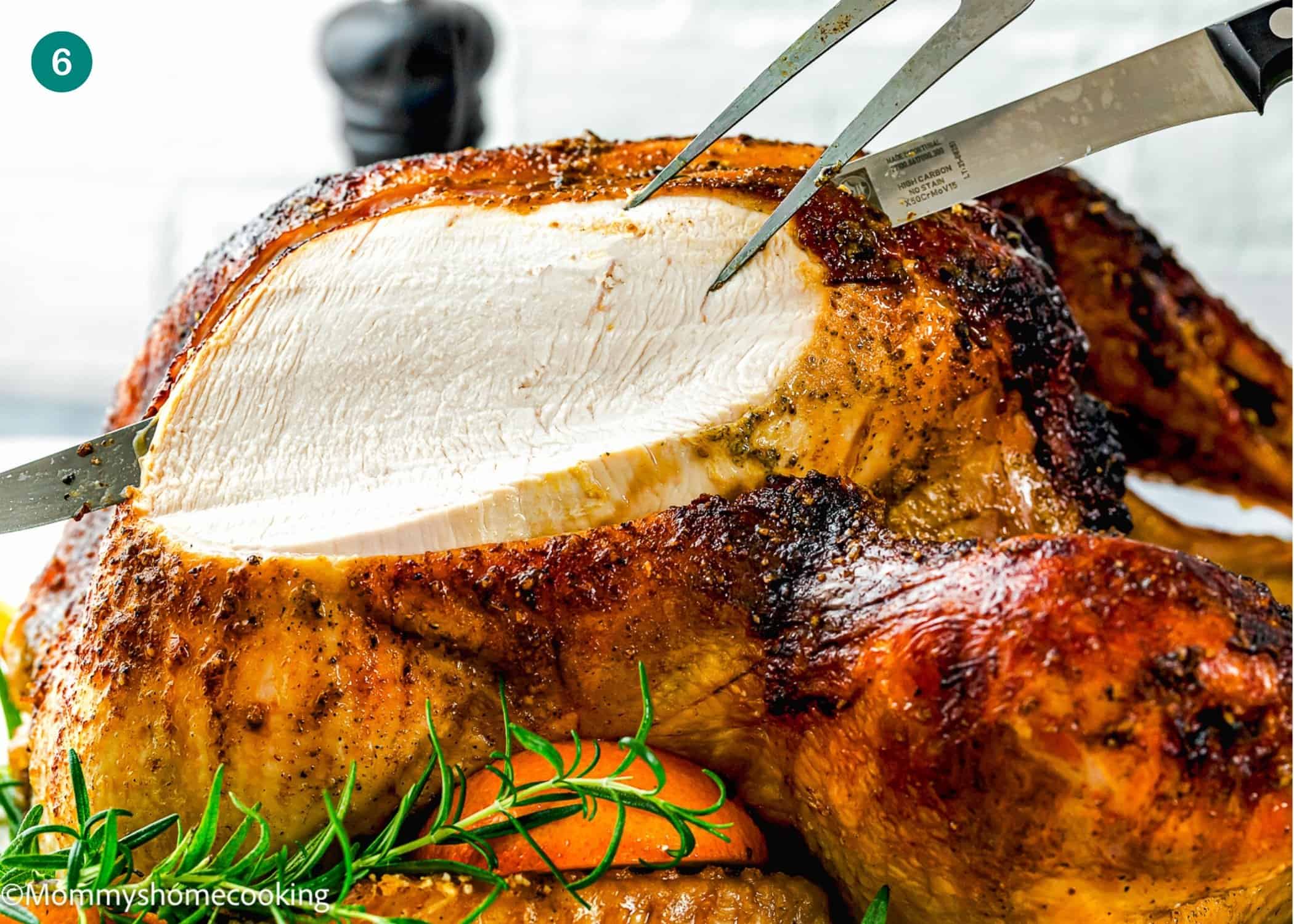 A whole roasted turkey being carved with a knife and fork, garnished with fresh rosemary and orange slices—a delicious Citrus-Garlic Chipotle Thanksgiving Turkey Recipe centerpiece.