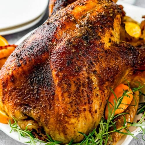A whole roasted turkey with crispy, seasoned skin is served on a platter garnished with fresh rosemary and orange slices—Not a Classic Boring Turkey: Citrus-Garlic Chipotle Thanksgiving Turkey Recipe.