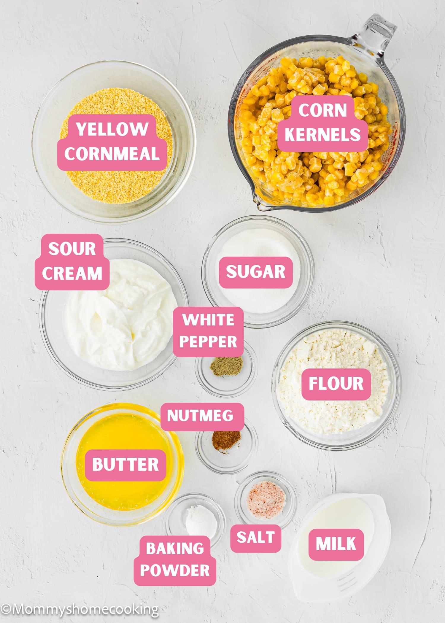 Top-down view of labeled ingredients for Easy Homemade Corn Pudding without Eggs: yellow cornmeal, corn kernels, sour cream, sugar, white pepper, nutmeg, flour, butter, salt, baking powder, and milk.