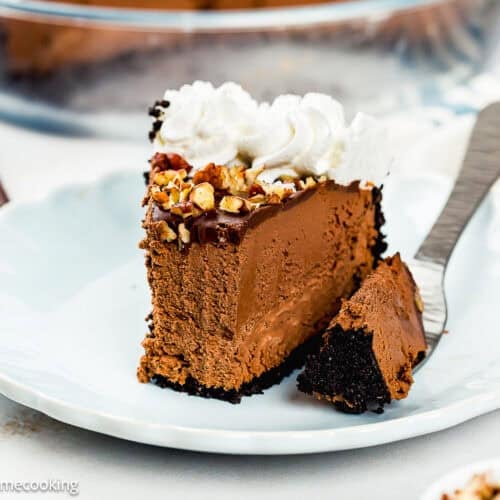 A slice of Eggless Chocolate Mousse Pie (no-bake) with whipped cream and chopped nuts on top, served on a white plate with a fork.