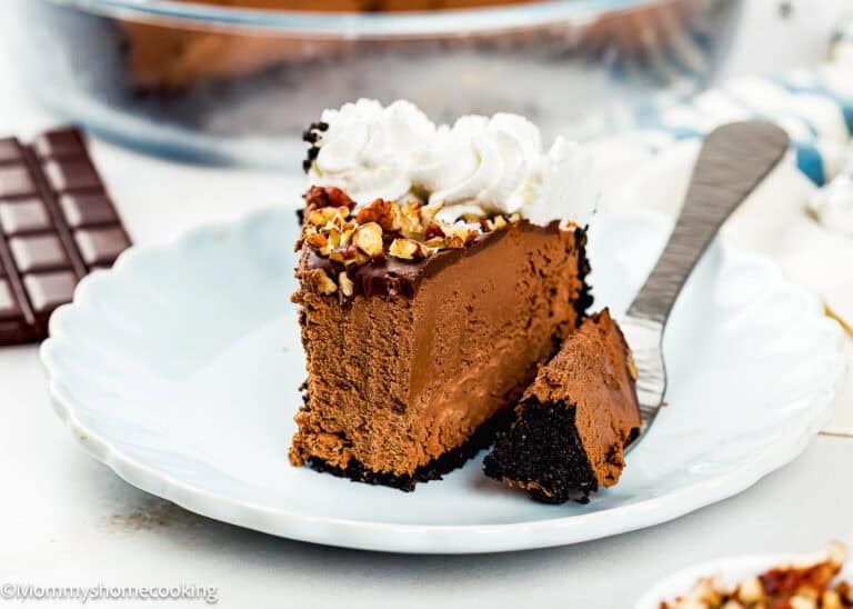 Top the slices of eggless chocolate mousse pie (no bake) with whipped cream and chopped nuts and serve with a fork on a white plate.