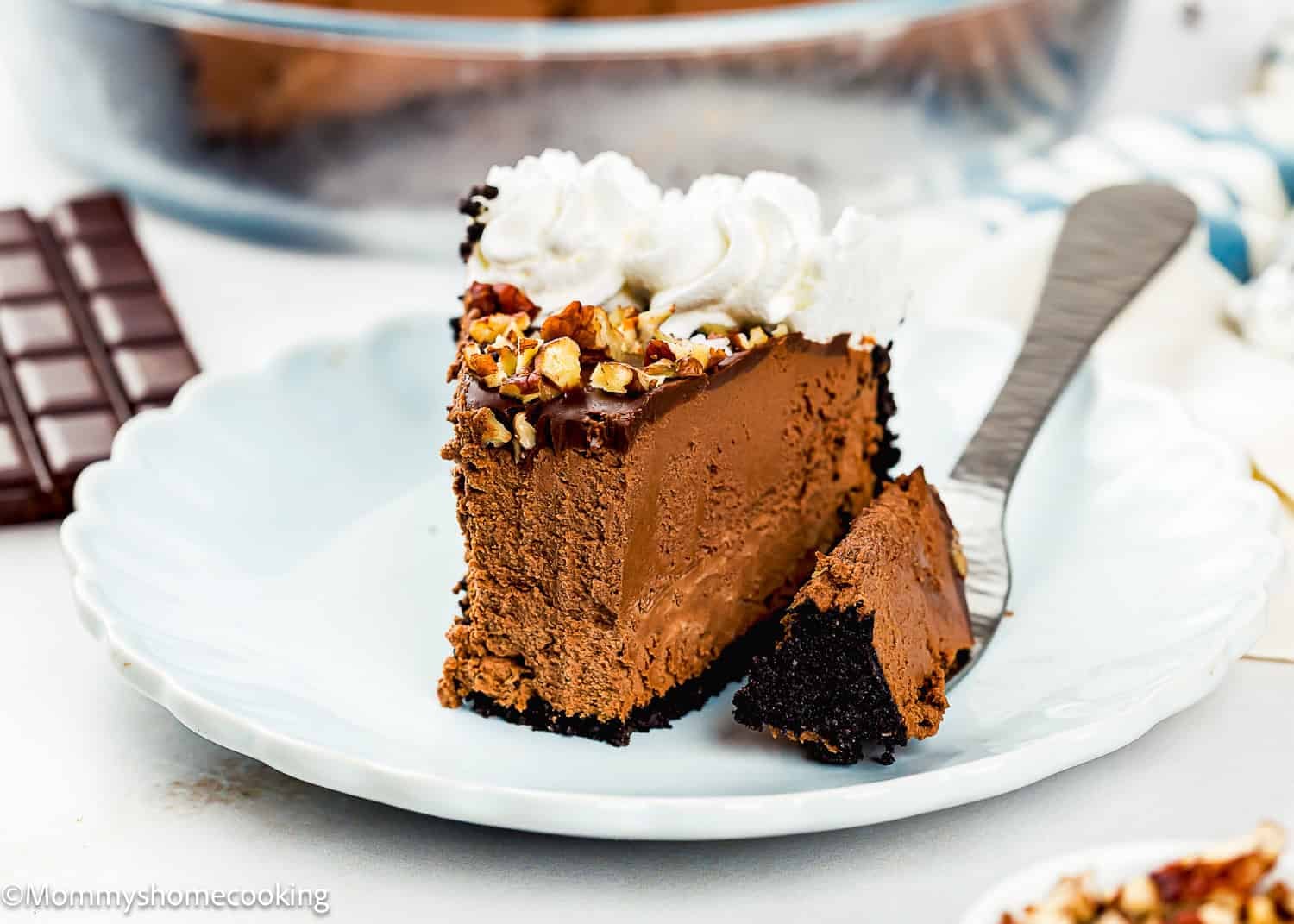 A slice of Eggless Chocolate Mousse Pie (no-bake) with whipped cream and chopped nuts on top, served on a white plate with a fork.