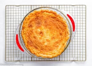 An Eggless Classic Chess Pie Recipe, baked to perfection with a golden-brown crust in a glass dish with red handles, cooling on a wire rack.