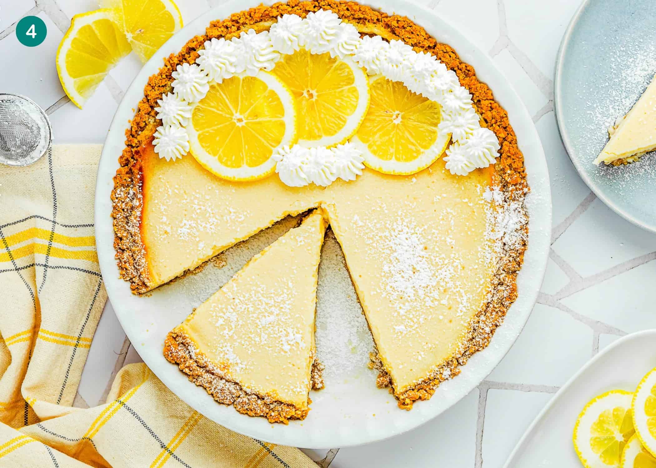 An Eggless Creamy Lemon Pie with a graham cracker crust, topped with whipped cream and lemon slices, sits on a plate with one slice removed.