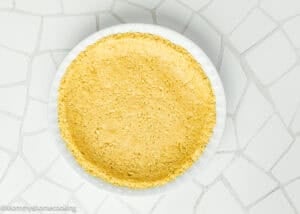 A white pie dish filled with an even layer of yellow, crumbly pie crust sits on a white, mosaic-tiled surface.