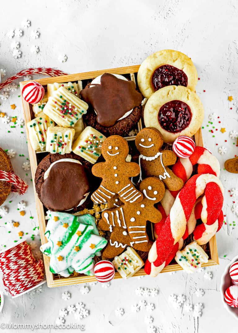 An Eggless Holiday Cookie Box filled with assorted festive treats, including gingerbread people, striped candy canes, decorated tree cookies, and thumbprint cookies with red jam.