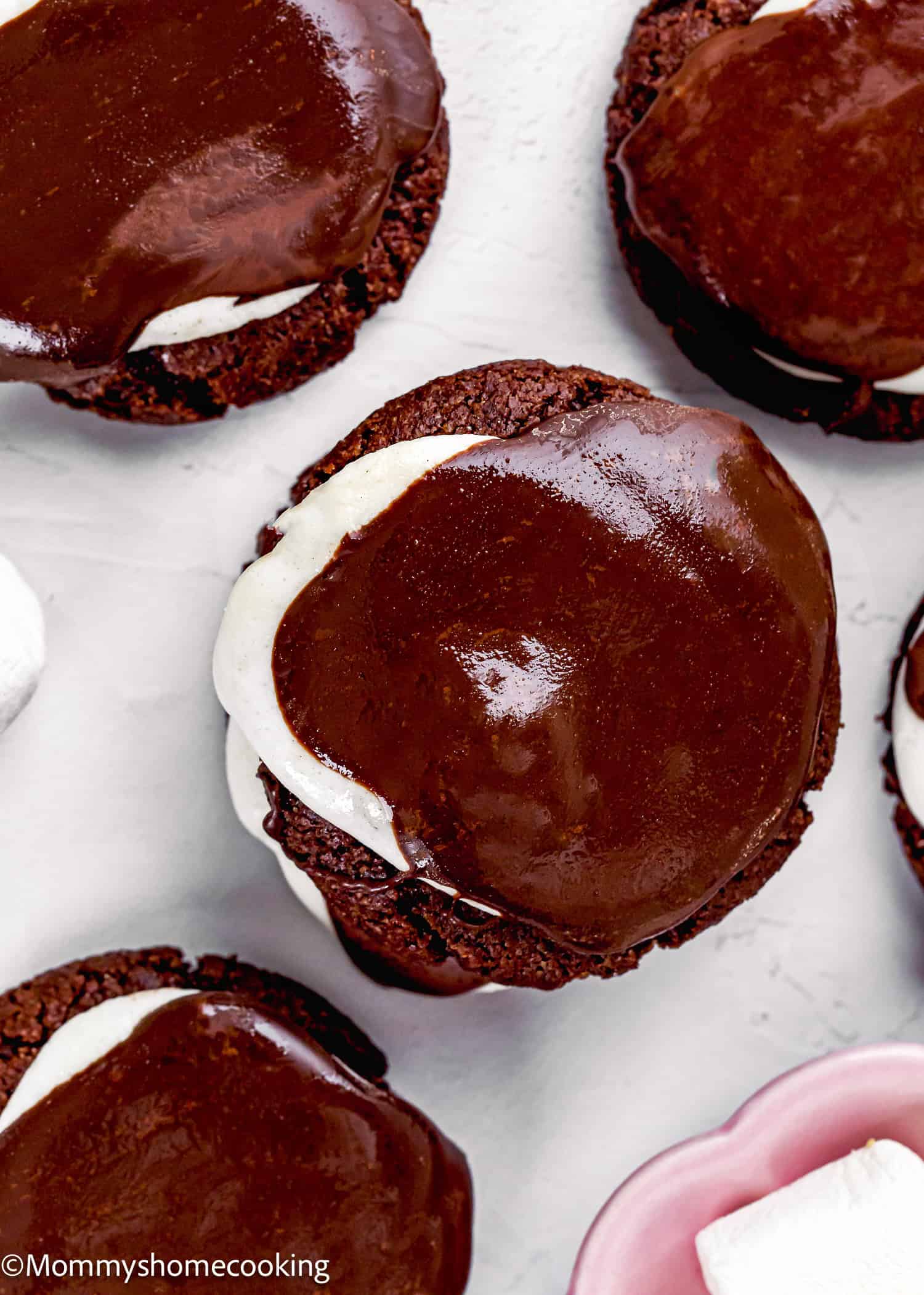 Close-up of Eggless Hot Chocolate Cookies topped with a layer of white marshmallow and glossy chocolate coating on a white surface.