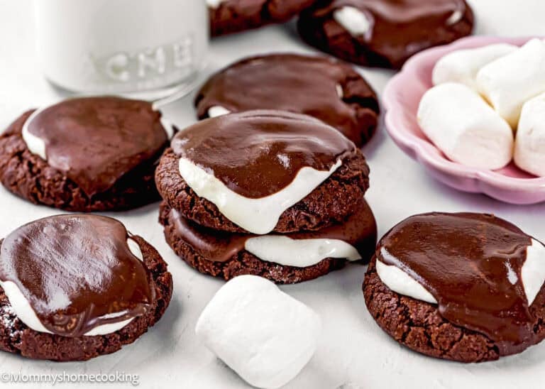 Eggless Hot Chocolate Cookies topped with toasted marshmallow and a layer of chocolate ganache, arranged beside marshmallows and a glass of milk.