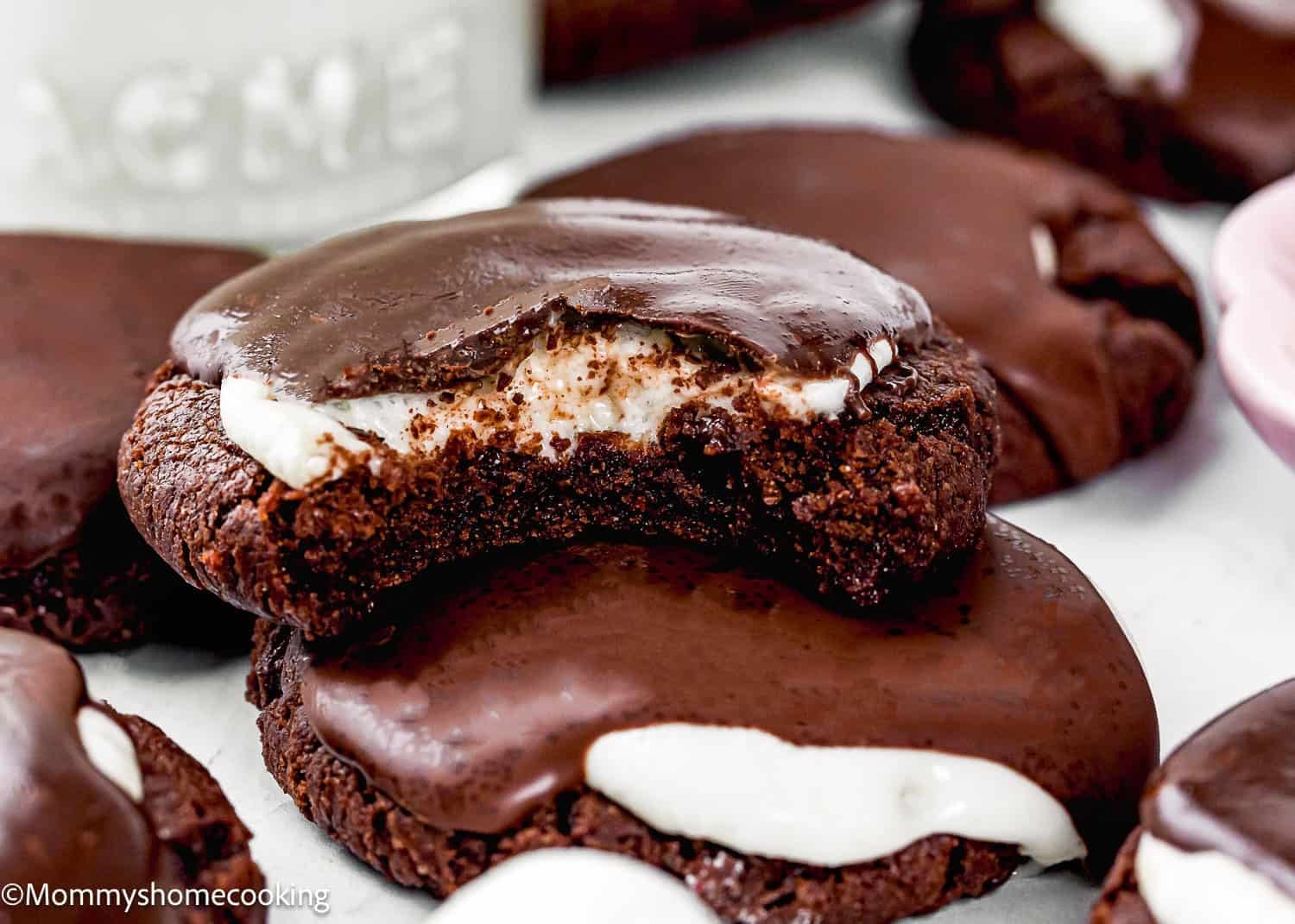 Close-up of Eggless Hot Chocolate Cookies with a creamy white filling, one cookie showing a bite taken out to reveal the inside.