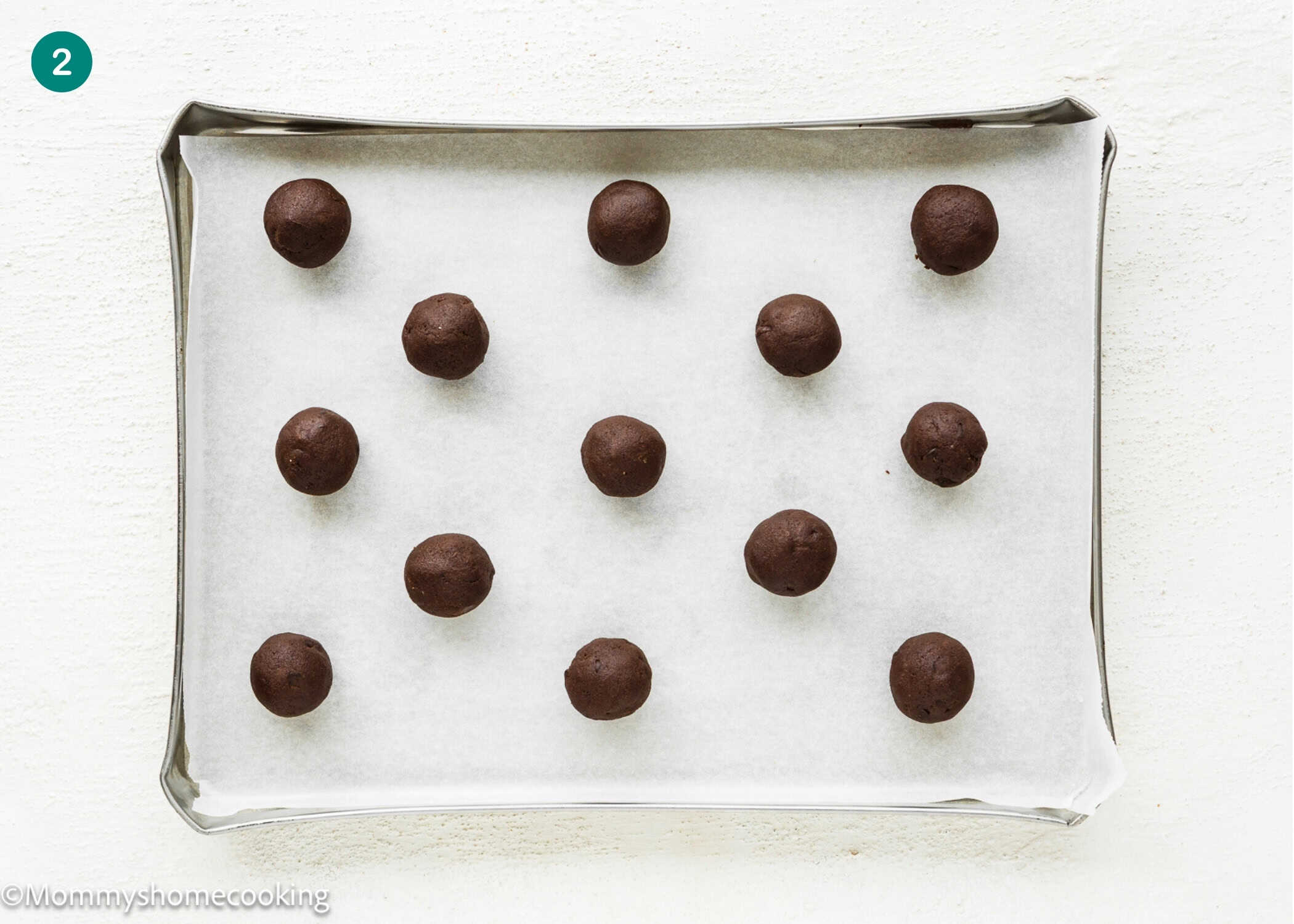 A baking sheet lined with parchment paper holds fifteen evenly spaced balls of Eggless Hot Chocolate Cookies dough.
