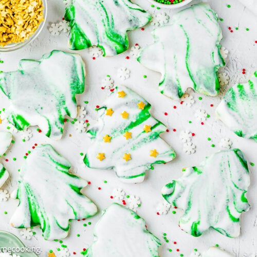 Eggless Marble Christmas Tree Cookies shaped like trees, decorated with white and green icing, and surrounded by red, green, and white sprinkles on a white surface.