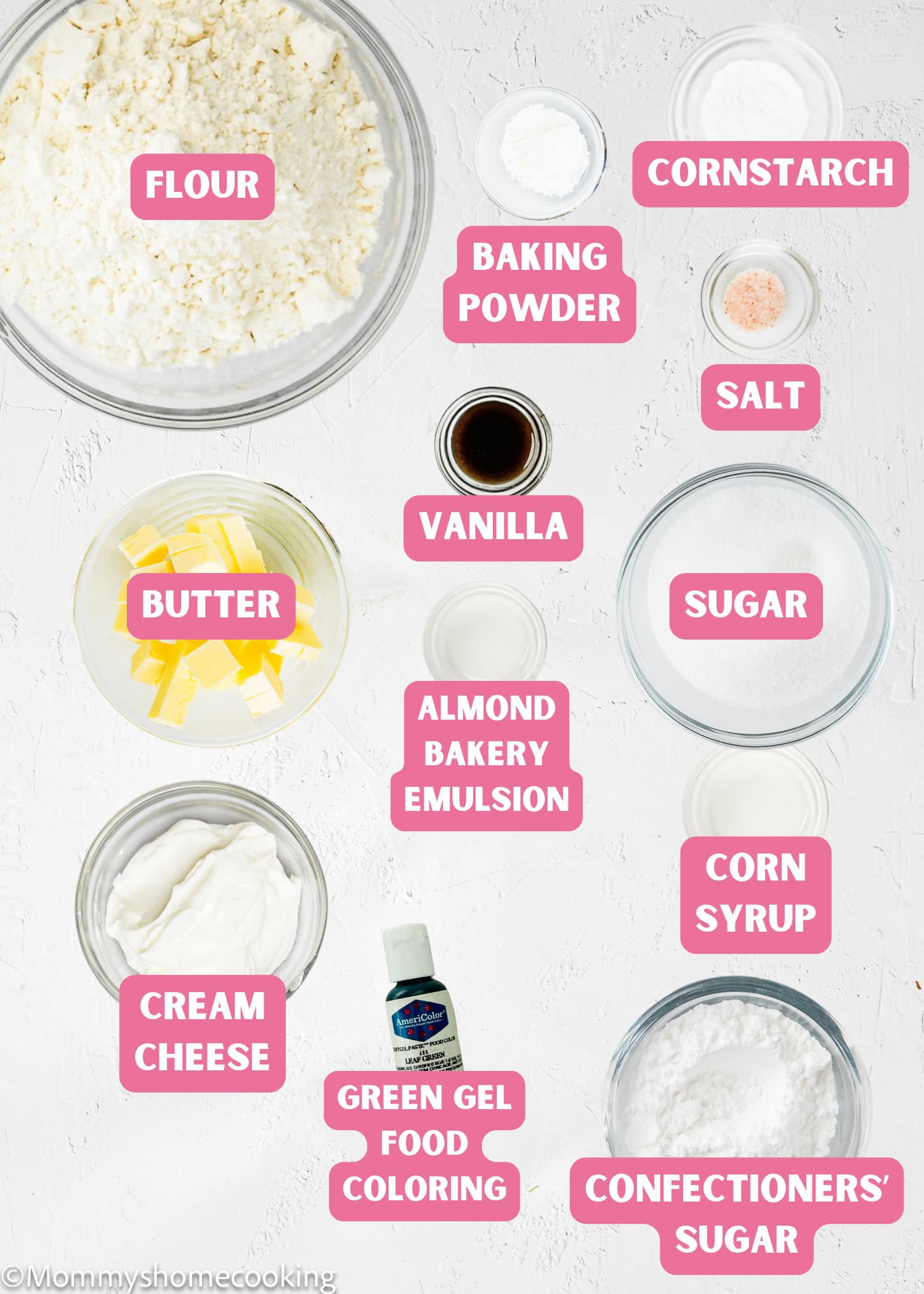 Various baking ingredients are arranged on a white surface and labeled, ready for making Eggless Marble Christmas Tree Cookies, including flour, butter, baking powder, cornstarch, salt, vanilla, sugar, and food coloring.