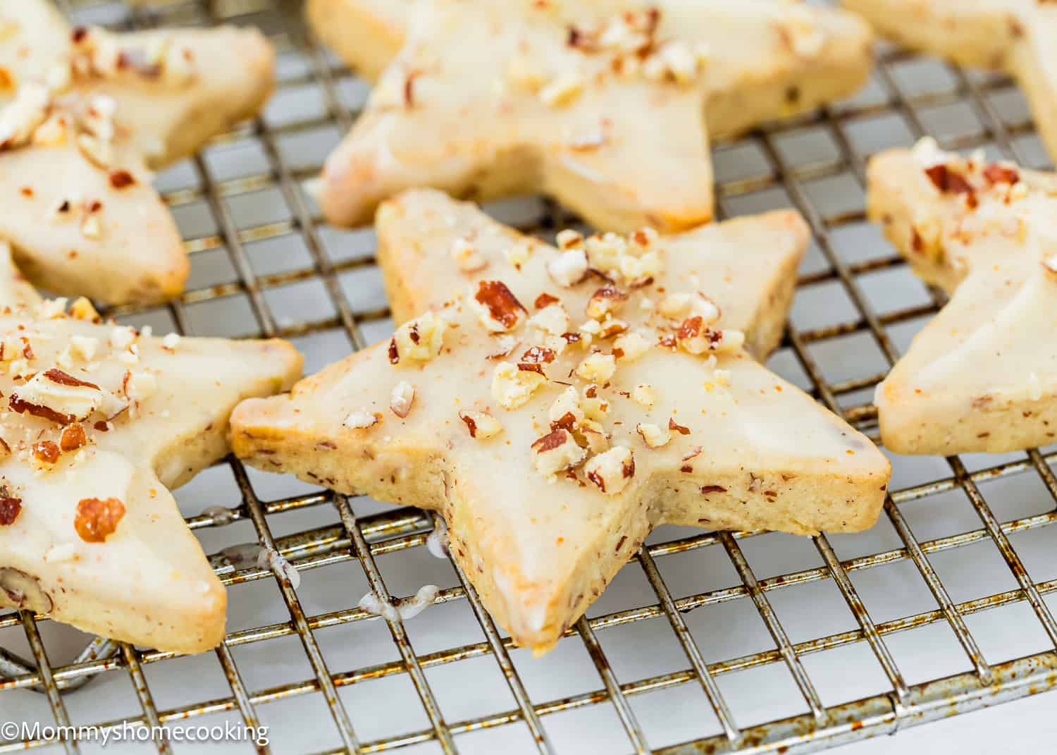Eggless Pecan Sugar Cookies with Brown Butter Icing are star-shaped, topped with chopped nuts, and cooling on a wire rack.