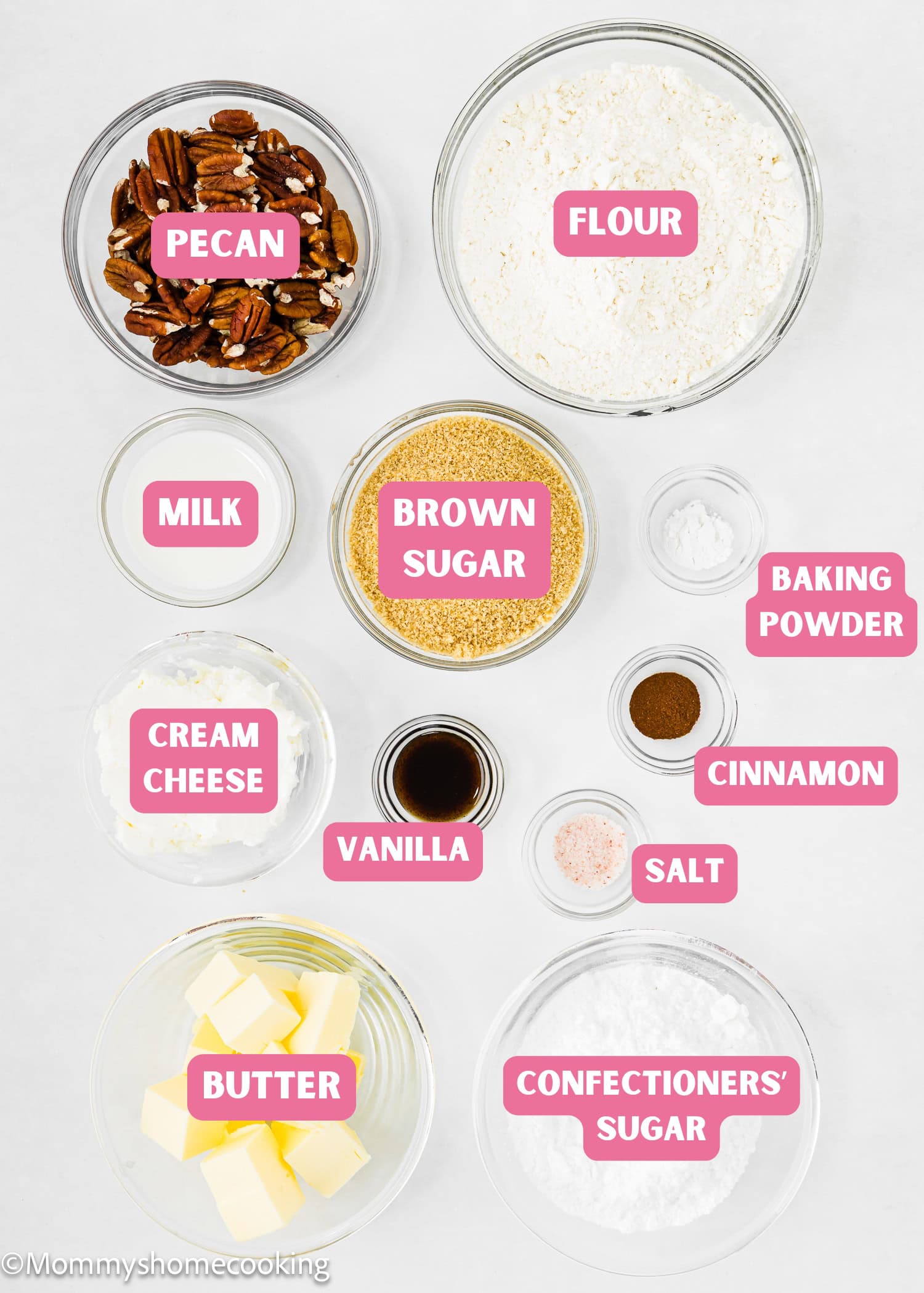 Top-down view of ingredients in bowls labeled for Eggless Pecan Sugar Cookies with Brown Butter Icing, including pecan, flour, milk, brown sugar, baking powder, cream cheese, cinnamon, vanilla, salt, butter, and confectioners’ sugar.