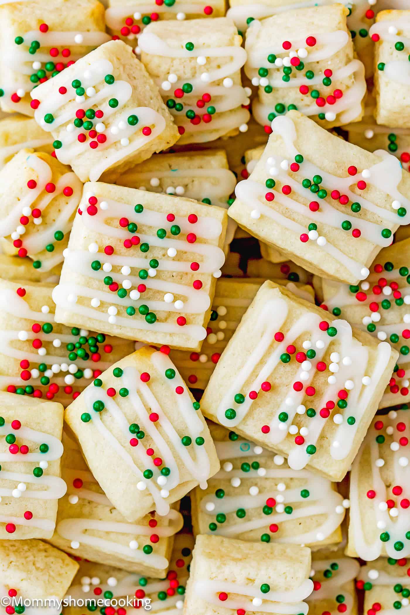 A pile of Eggless Sugar Cookie Bites topped with white icing and red, green, and white sprinkles.