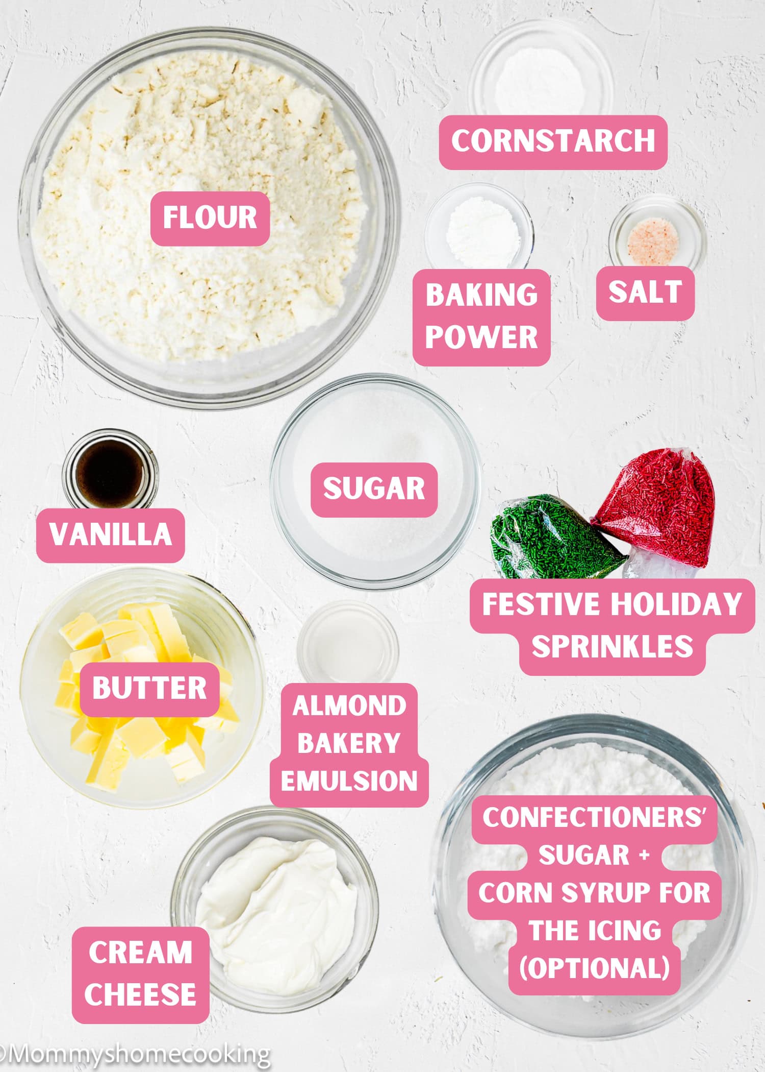 Top-down view of labeled baking ingredients for Eggless Sugar Cookie Bites in bowls, including flour, sugar, butter, cream cheese, baking powder, salt, vanilla, almond emulsion, cornstarch, sprinkles, and icing ingredients.