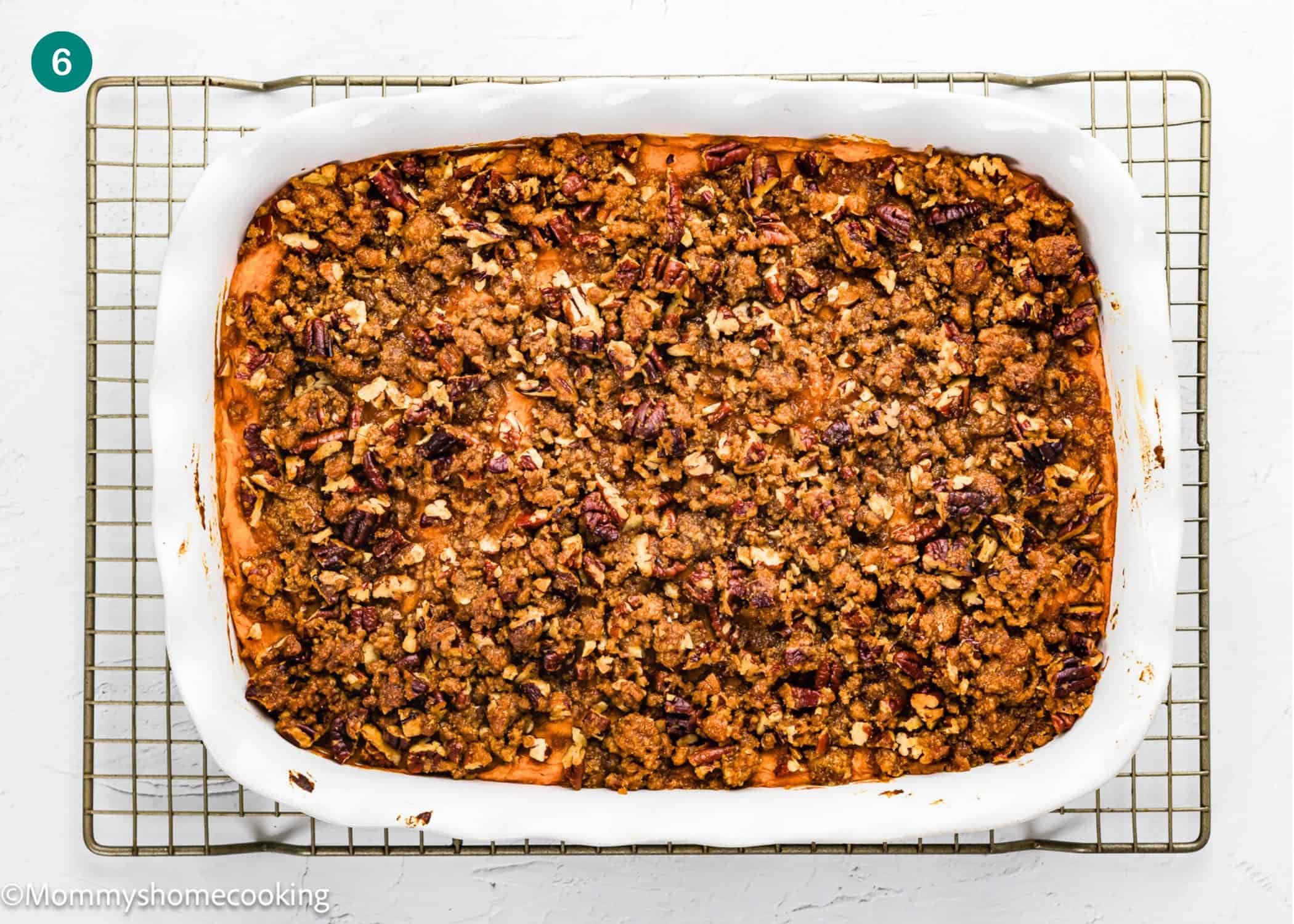 Rectangular white baking dish filled with an eggless sweet potato casserole topped with pecans, placed on a wire cooling rack against a white background.