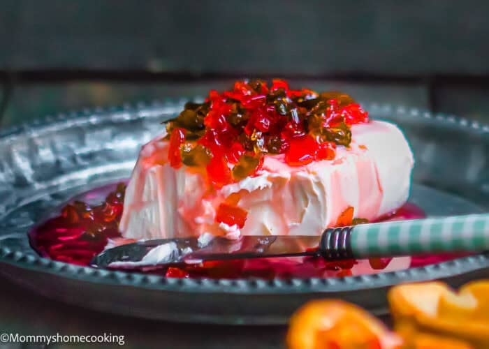 A block of cream cheese topped with hot pepper jelly sits on a metal plate, making the perfect Hot Pepper Jelly Cream Cheese Appetizer (Sweet & Spicy!). A knife rests beside it for easy serving.