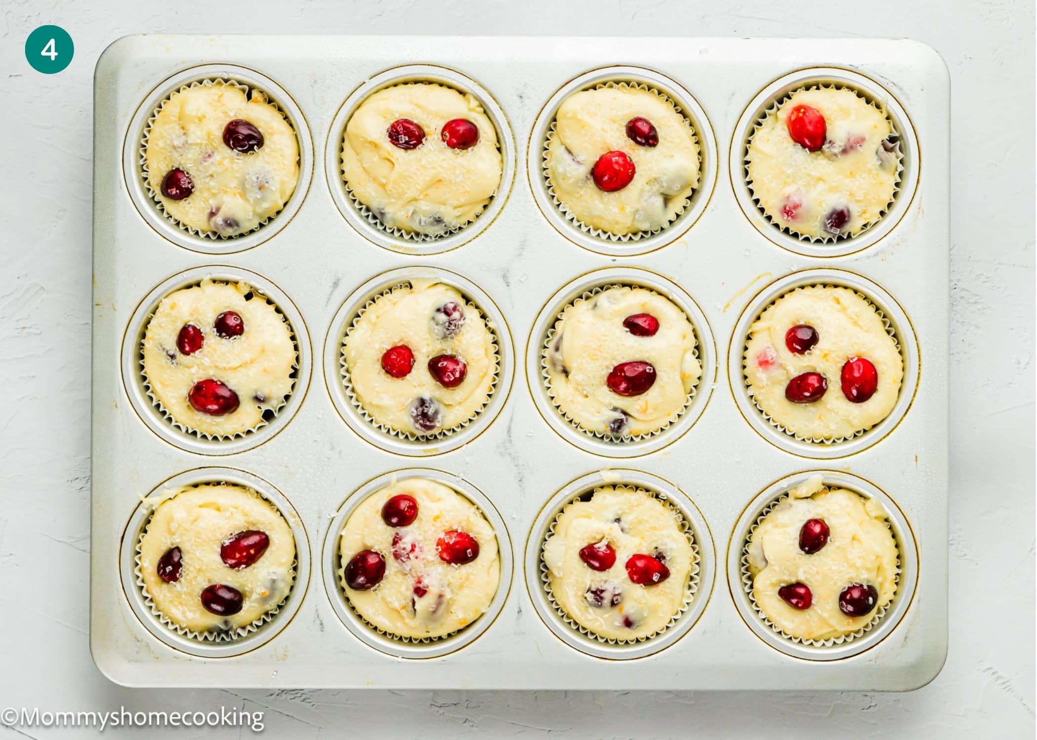 A muffin pan filled with raw Cranberry Orange Muffins without Eggs batter, featuring visible whole cranberries, sits on a white surface ready to be baked.