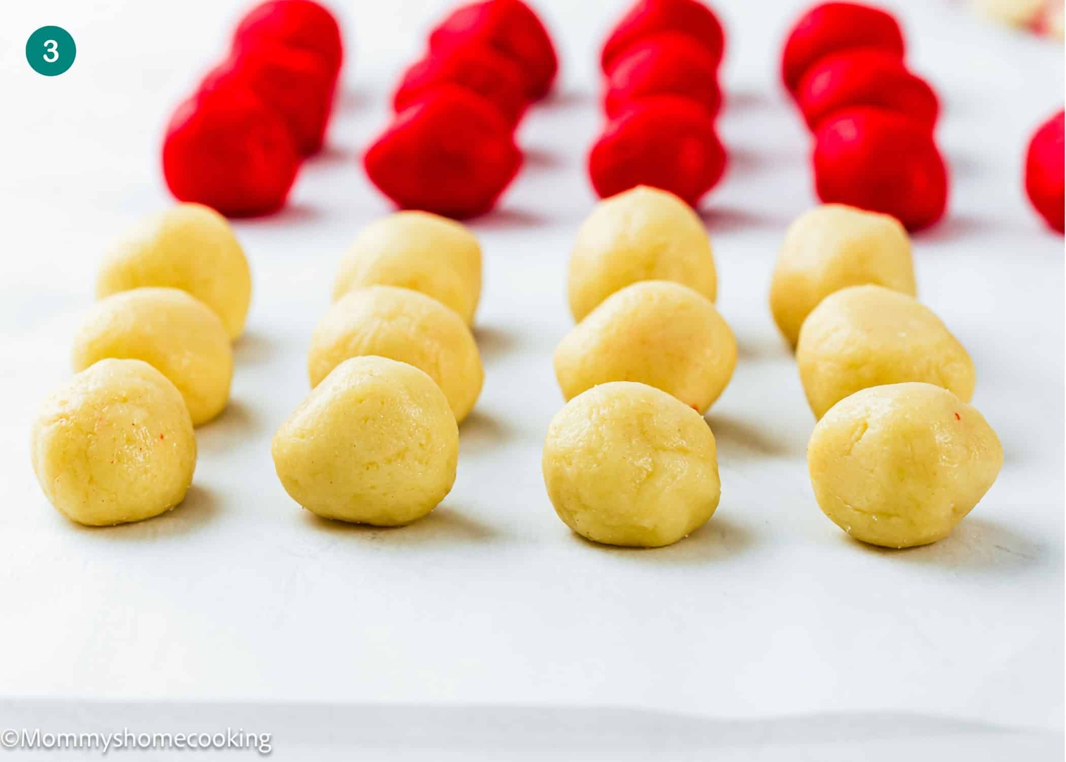 Rows of unbaked dough balls, yellow in front and red in back, arranged on a white surface for Eggless Candy Canes Cookies.