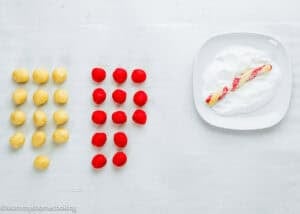 Rows of yellow and red cookie dough balls are on the left; on the right, an Eggless Candy Canes Cookies dough strand is twisted and coated in sugar on a white plate.