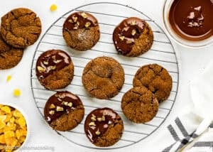 A cooling rack holds nine Eggless Chocolate Ginger Cookies, some half-dipped in chocolate and topped with candied ginger; a bowl of melted chocolate and a bowl of chopped ginger sit nearby.