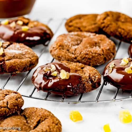 Eggless Chocolate Ginger Cookies, some half-dipped in chocolate and sprinkled with chopped nuts or fruit, cool on a wire rack.