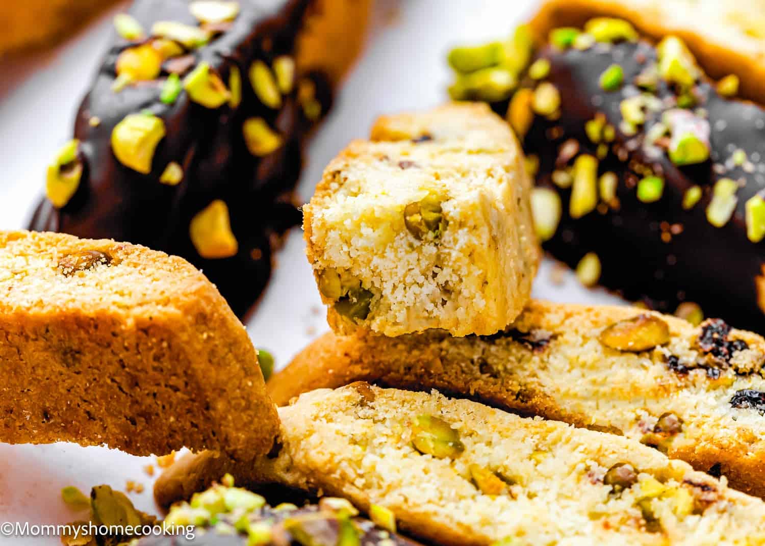 Close-up of sliced biscotti with visible pistachios, some pieces dipped in chocolate and sprinkled with chopped pistachios—a delicious Eggless Easy Biscotti Recipe.