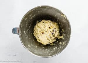 A metal mixing bowl containing a ball of cookie dough with visible chocolate chips sits on a white surface, perfect for an eggless easy biscotti recipe.