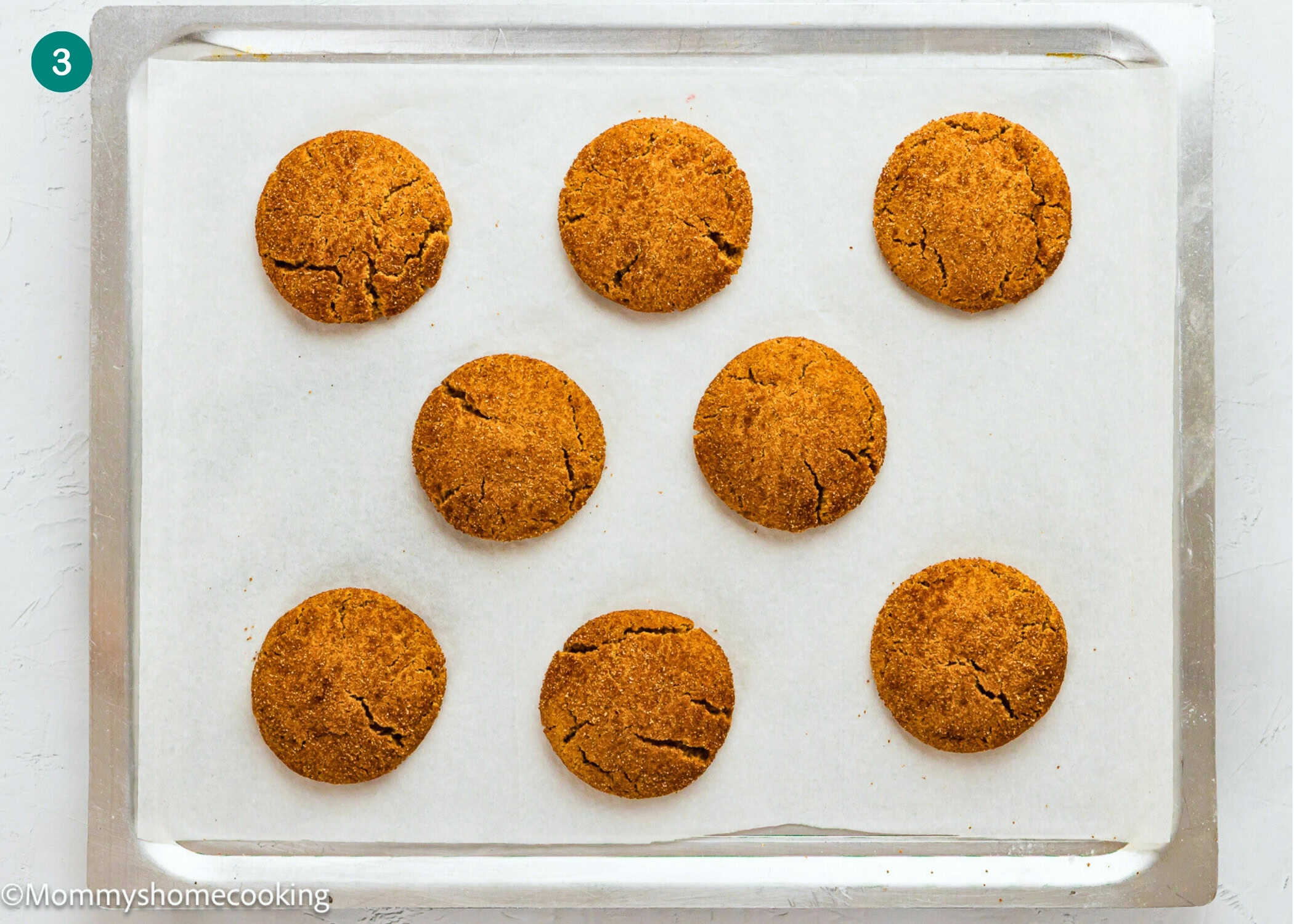 Eight round Eggless Gingerbread Snickerdoodle cookies are evenly spaced on a parchment-lined baking sheet.