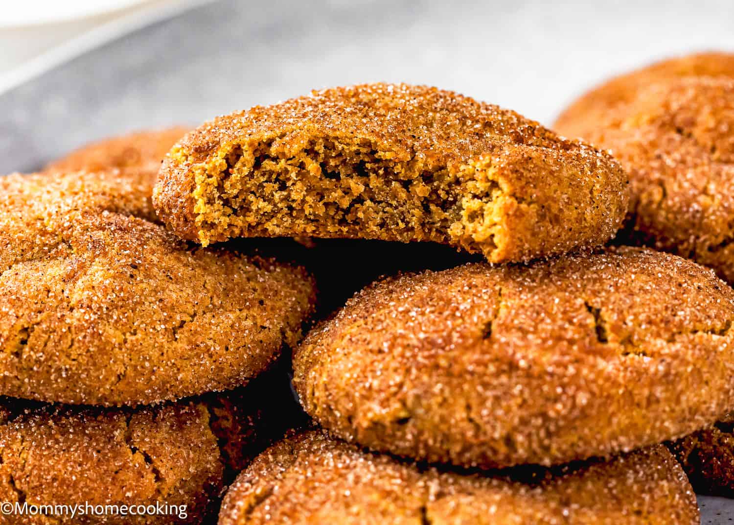 A close-up of several eggless gingerbread snickerdoodle cookies, with one cookie broken in half to show its soft interior.