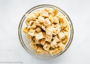 A glass bowl filled with cubes of sliced bread on a white surface, perfect for making an Eggless Strata Recipe.