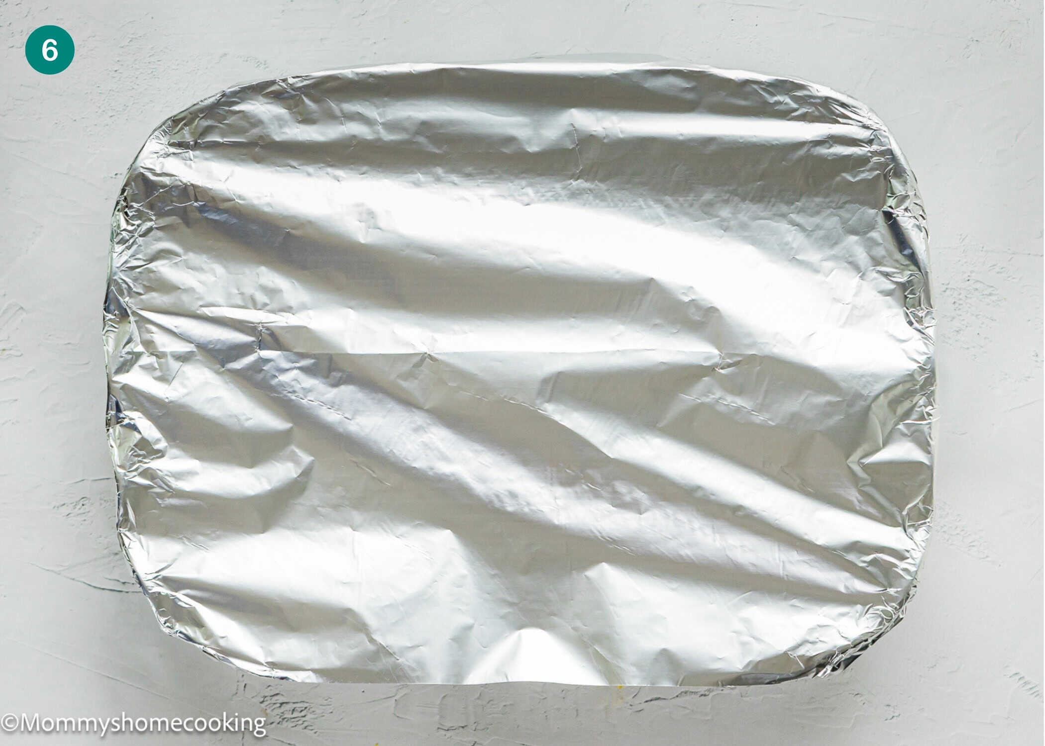 A rectangular baking dish covered tightly with aluminum foil sits on a light-colored surface, ready for your Eggless Strata Recipe.