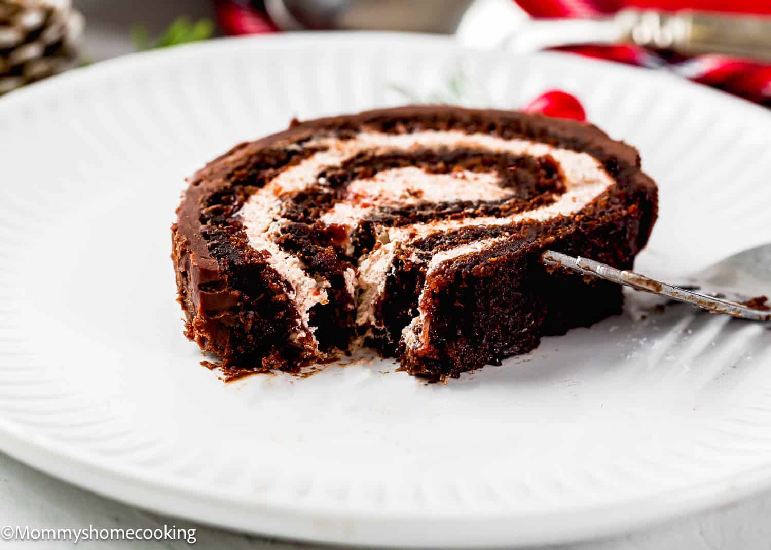 A partially eaten slice of Egg-Free Yule Log (Bûche De Noël) with cream filling sits on a white plate, with a fork resting beside it.