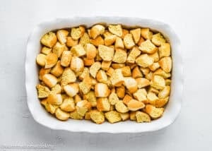 A white baking dish filled with evenly spread chunks of cubed bread on a white surface, perfect for preparing Overnight French Toast Casserole Without Eggs.