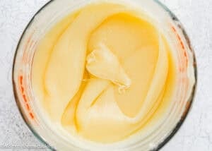 A close-up view of thick, creamy condensed milk in a glass measuring cup on a light surface, perfect for creating an easy cream cheese glaze.